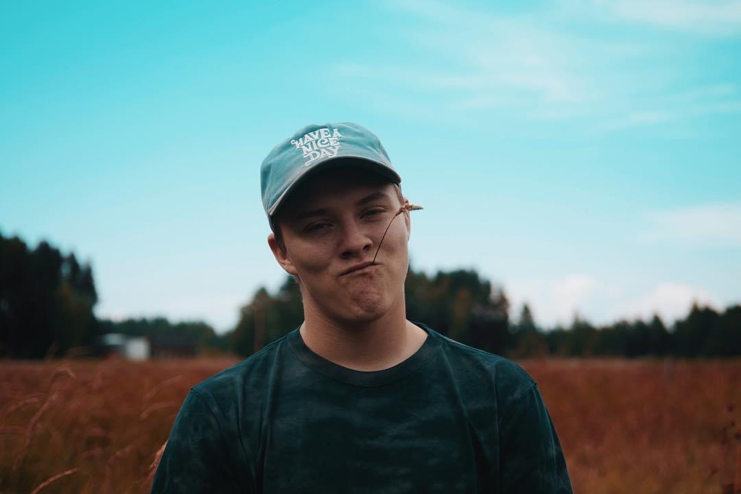 Dameon Spencer in a field wearing a Have a Nice Day cap